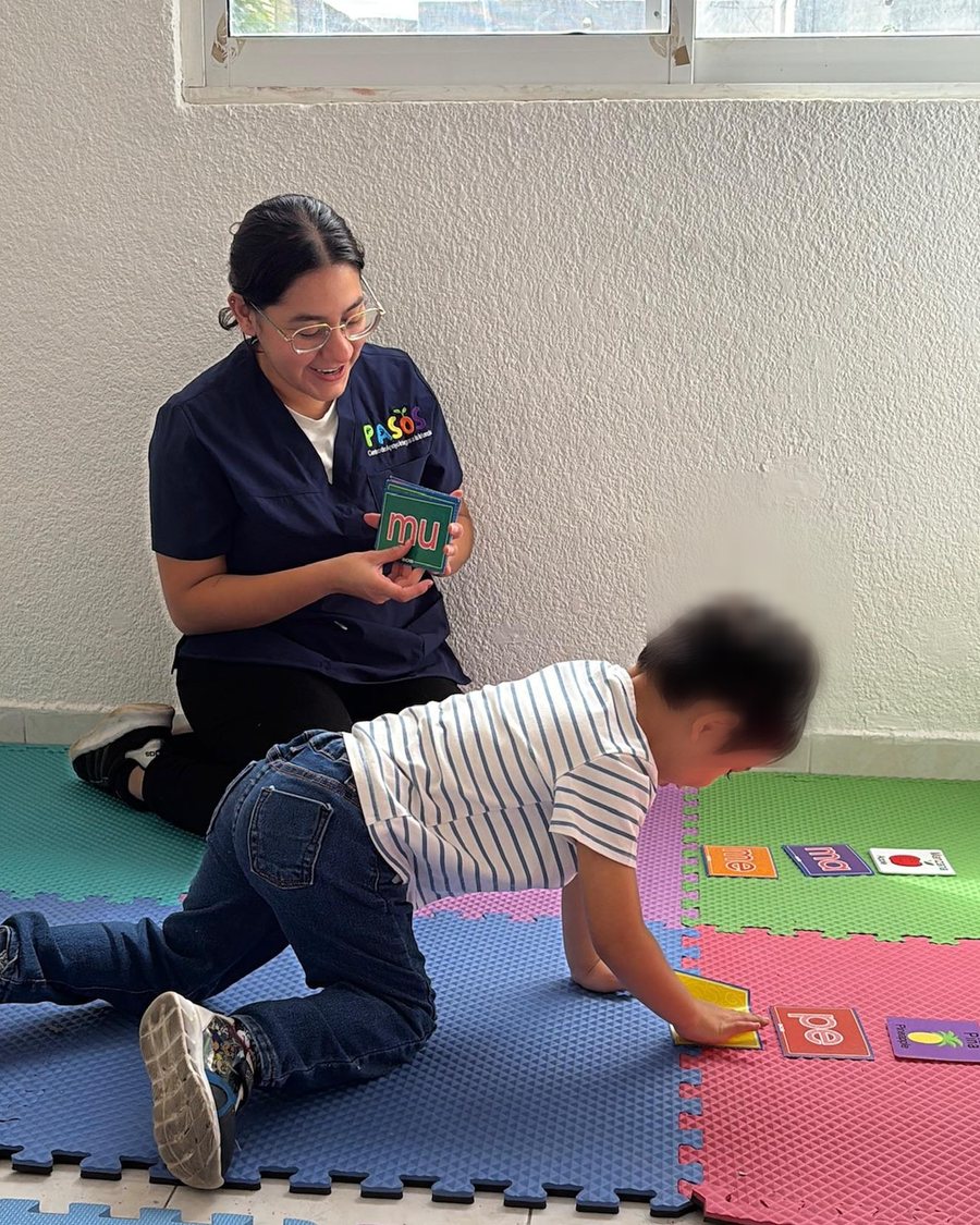 Instructora de PASOS trabajando de cerca con un niño sobre un tapete sensorial, usando tarjetas de sílabas